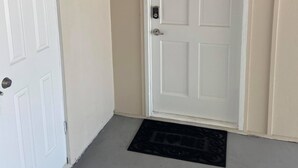 Une porte blanche dotée d’un clavier pour ouvrir, un paillasson noir et des murs de couleur beige.