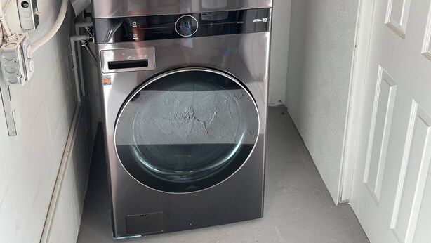 Un lave-linge et un sèche-linge LG ThinQ compacts, en acier inoxydable, installés dans un petit espace buanderie fermé, avec une porte blanche et des murs de couleur claire.