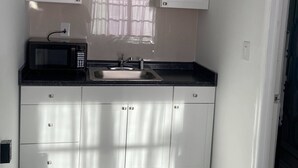 Une petite cuisine avec des meubles blancs, un plan de travail noir, un four à micro-ondes et un évier.