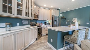 Une cuisine moderne avec des meubles en bois clair, un îlot central, des appareils en acier inoxydable et un mur d’accent de couleur turquoise.