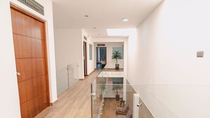 Un interior moderno con suelo de madera, barandilla de cristal y una planta en maceta.