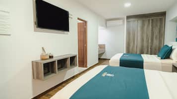 A hotel room with two beds, a flat-screen TV mounted on the wall, a wooden wardrobe, and a small shelf with a bottle and glasses.