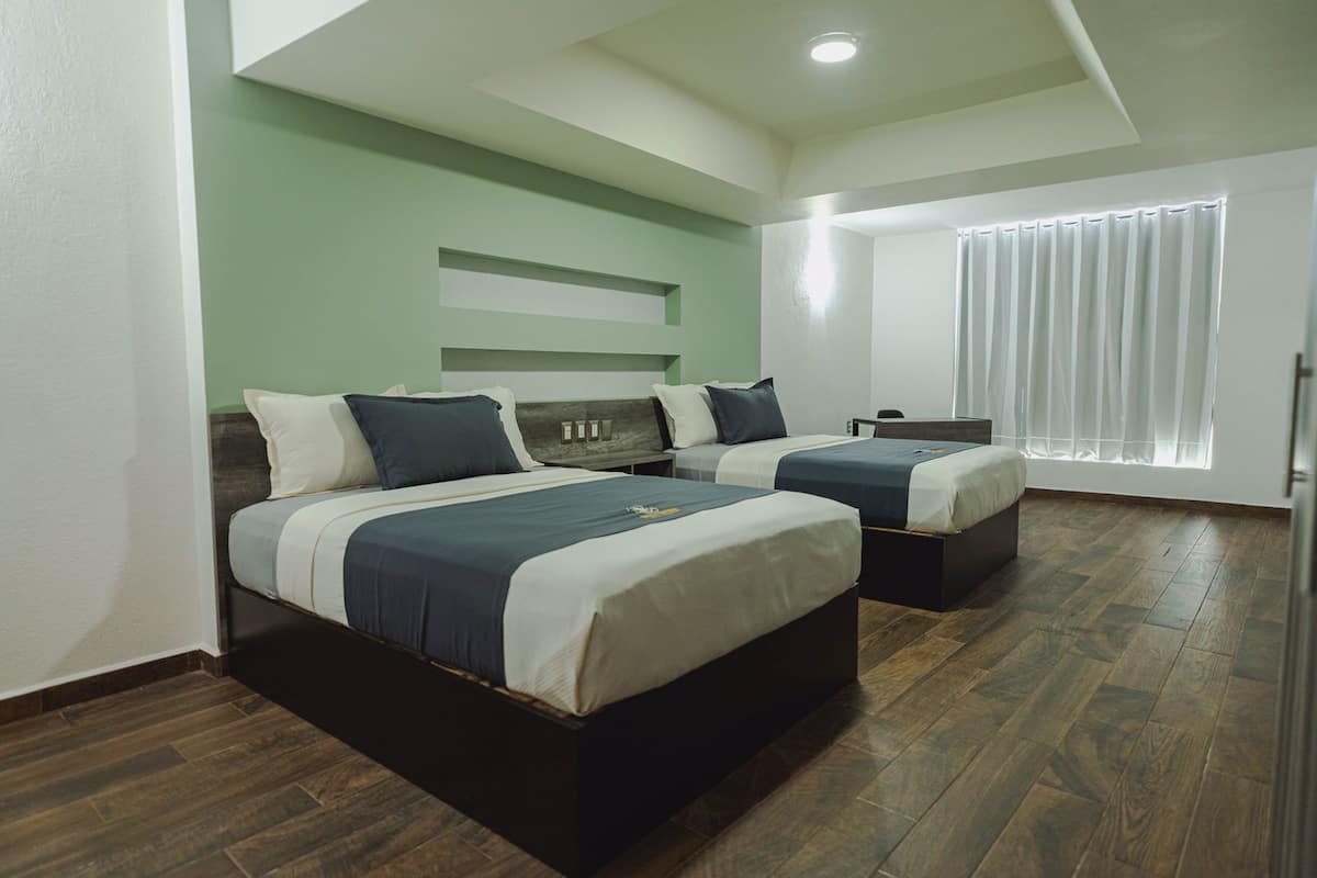 Une chambre d’hôtel avec deux lits, un bureau et une fenêtre avec des rideaux.