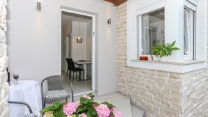 En lille terrasse med et bord og stole, et vindue med en plante, og en dør der fører ind.
