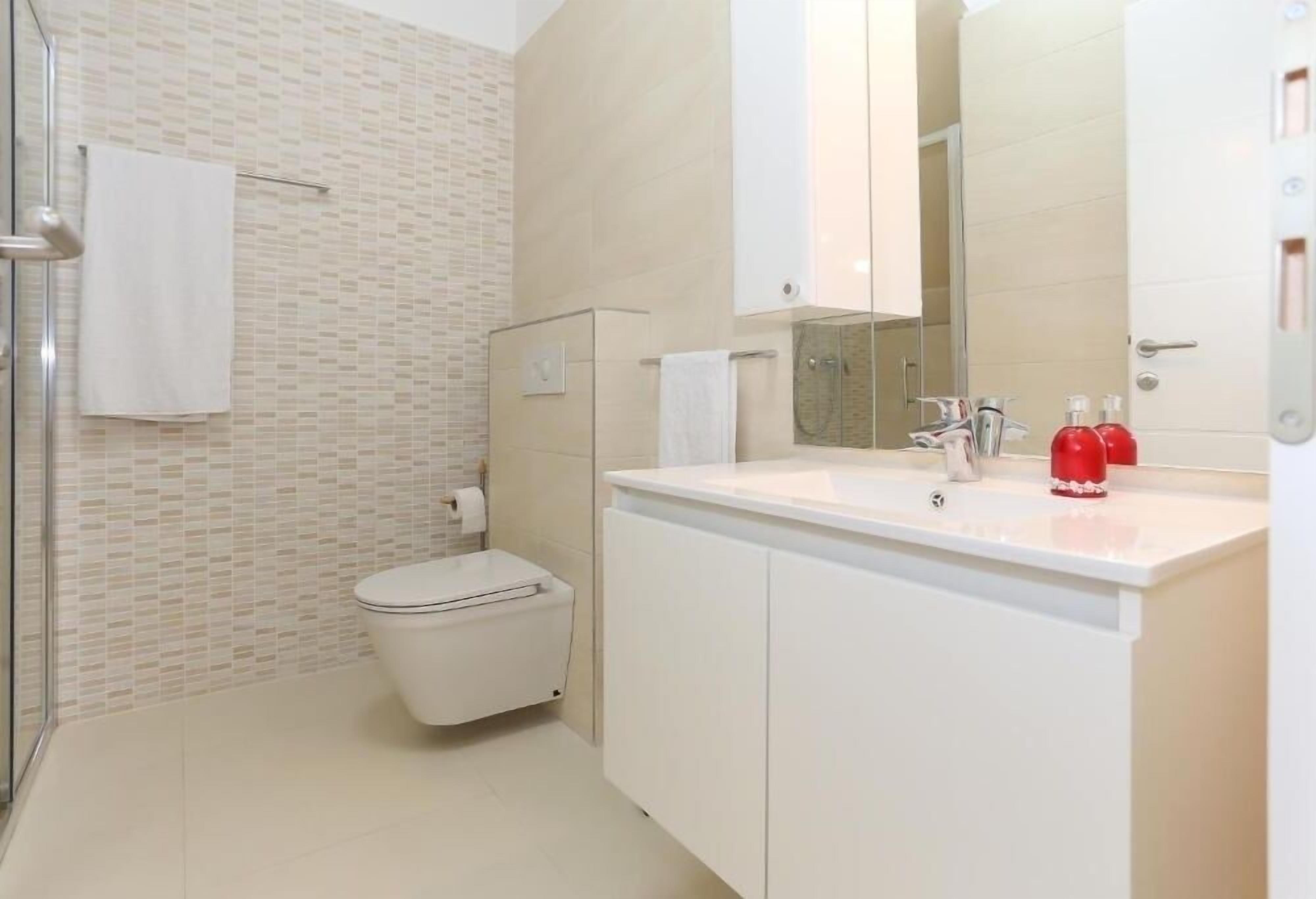Ein modernes Badezimmer mit einer Duschkabine aus Glas, einer weißen Toilette und einem Waschtisch mit Spiegel.