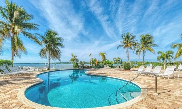 A pool area with a clear blue pool, palm trees, and lounge chairs.