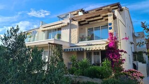 Une maison à deux étages dotée d’un balcon, d’une façade en pierre et d’un jardin où poussent des fleurs roses.
