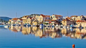 Une ville côtière aux bâtiments en pierre, un port de plaisance avec des bateaux et une eau calme qui reflète l’architecture.