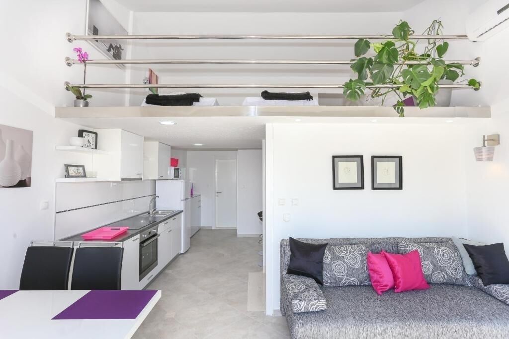 A modern apartment with a kitchen, dining area, and a living room with a sofa and a plant.