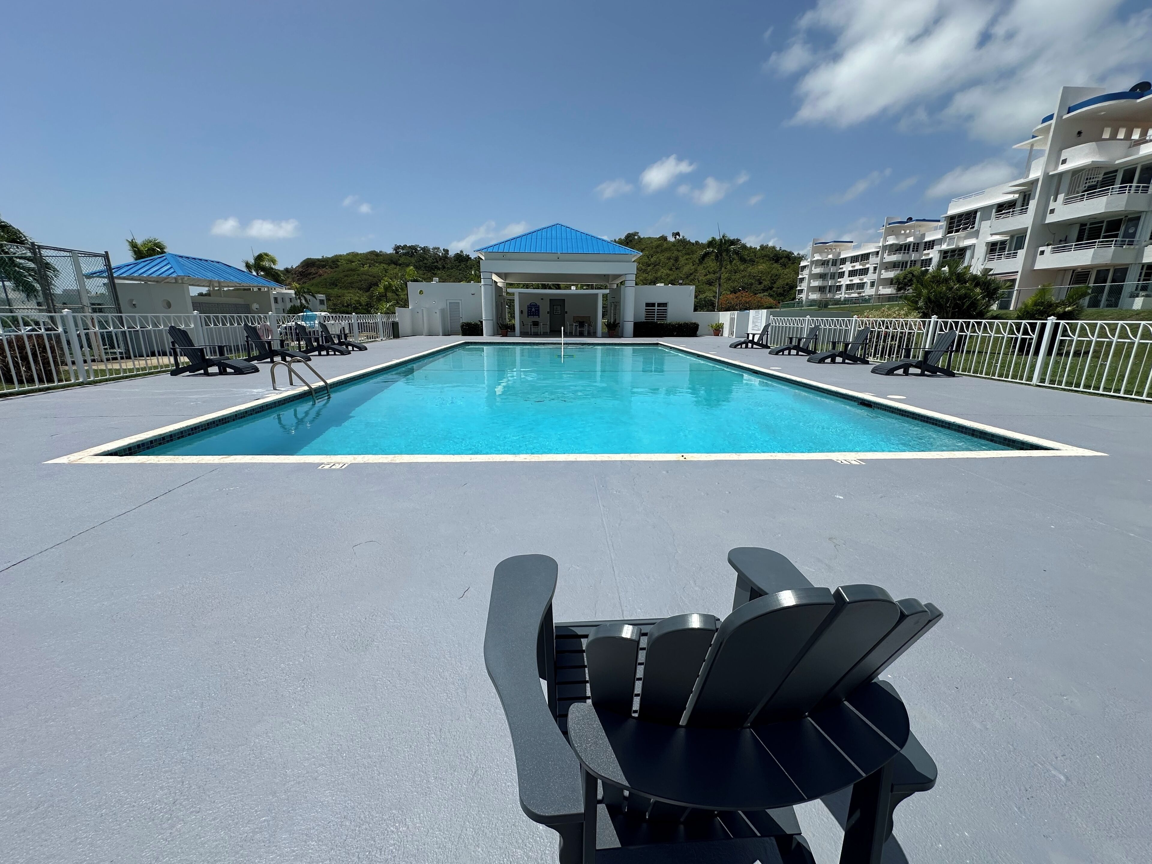 Ein Swimmingpool mit Liegestühlen und ein Gebäude mit blauem Dach im Hintergrund.