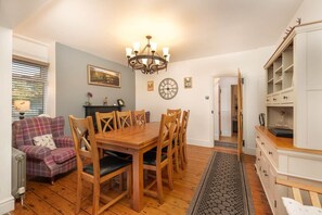 Een eetgedeelte met een houten tafel en stoelen, een kroonluchter en een klok aan de muur.
