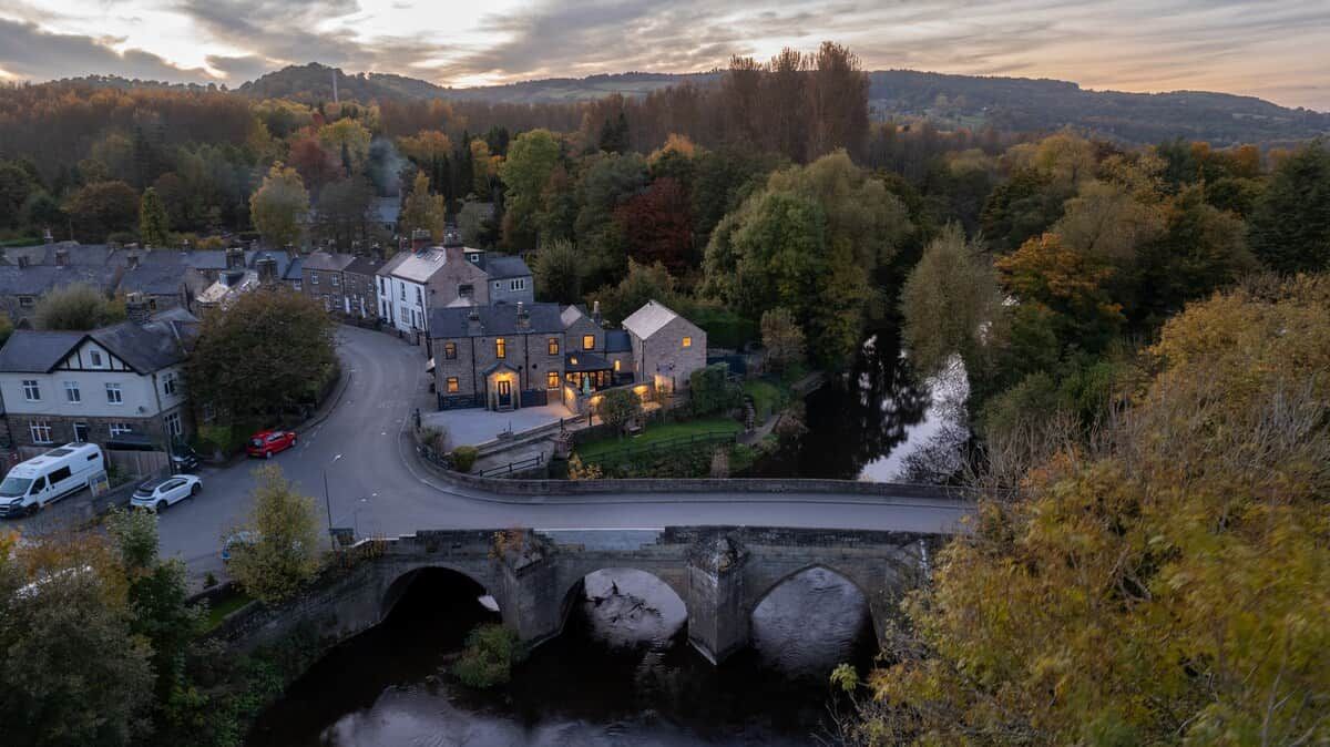A residential area with a prominent house featuring a stone bridge, a road, and a river.