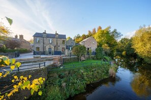 A stone building with a paved patio and a small bridge over a water channel. - Family Home | River Derwent | Hot tub | 10 guests (Darley Bridge)