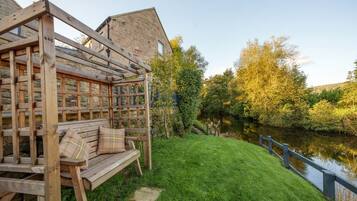 A wooden bench with cushions, a stone wall, and a view of a river.