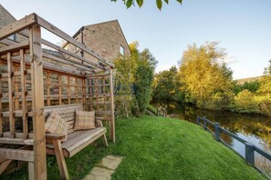 A wooden bench with cushions, a stone wall, and a view of a river. - Family Home | River Derwent | Hot tub | 10 guests (Darley Bridge)