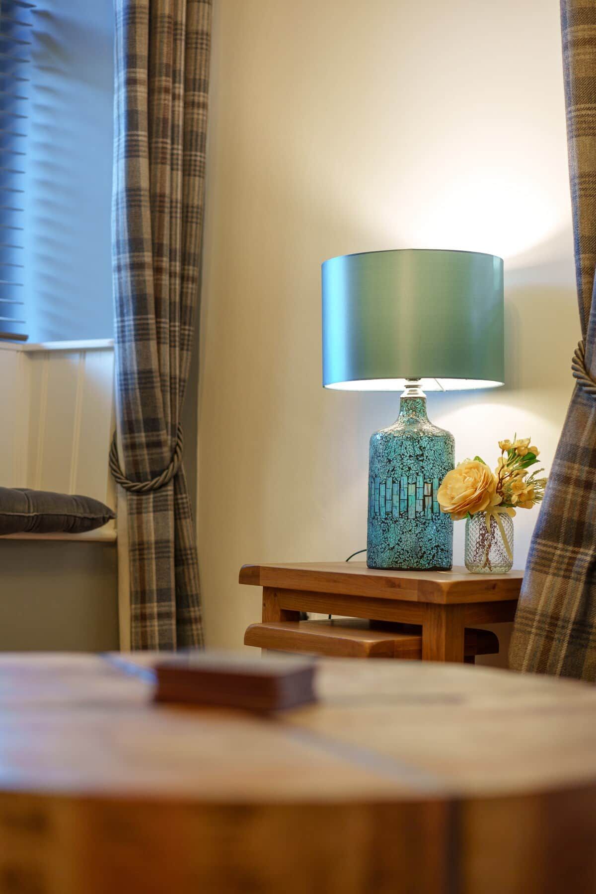 A room with a round wooden table, a lamp, and a vase with flowers.