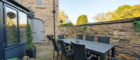 A patio with a table and chairs, a stone wall, and a building with a window and door.