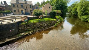 Eine Steinbrücke über einem ruhigen Fluss, umgeben von üppigem Grün und traditionellen Steinbauten.