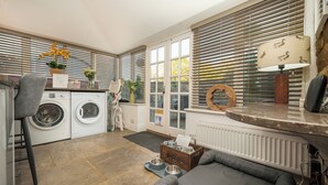 Ein Waschbereich mit Waschmaschine und Trockner, ein graues Sofa und eine Holzkiste mit Futternäpfen für Haustiere.