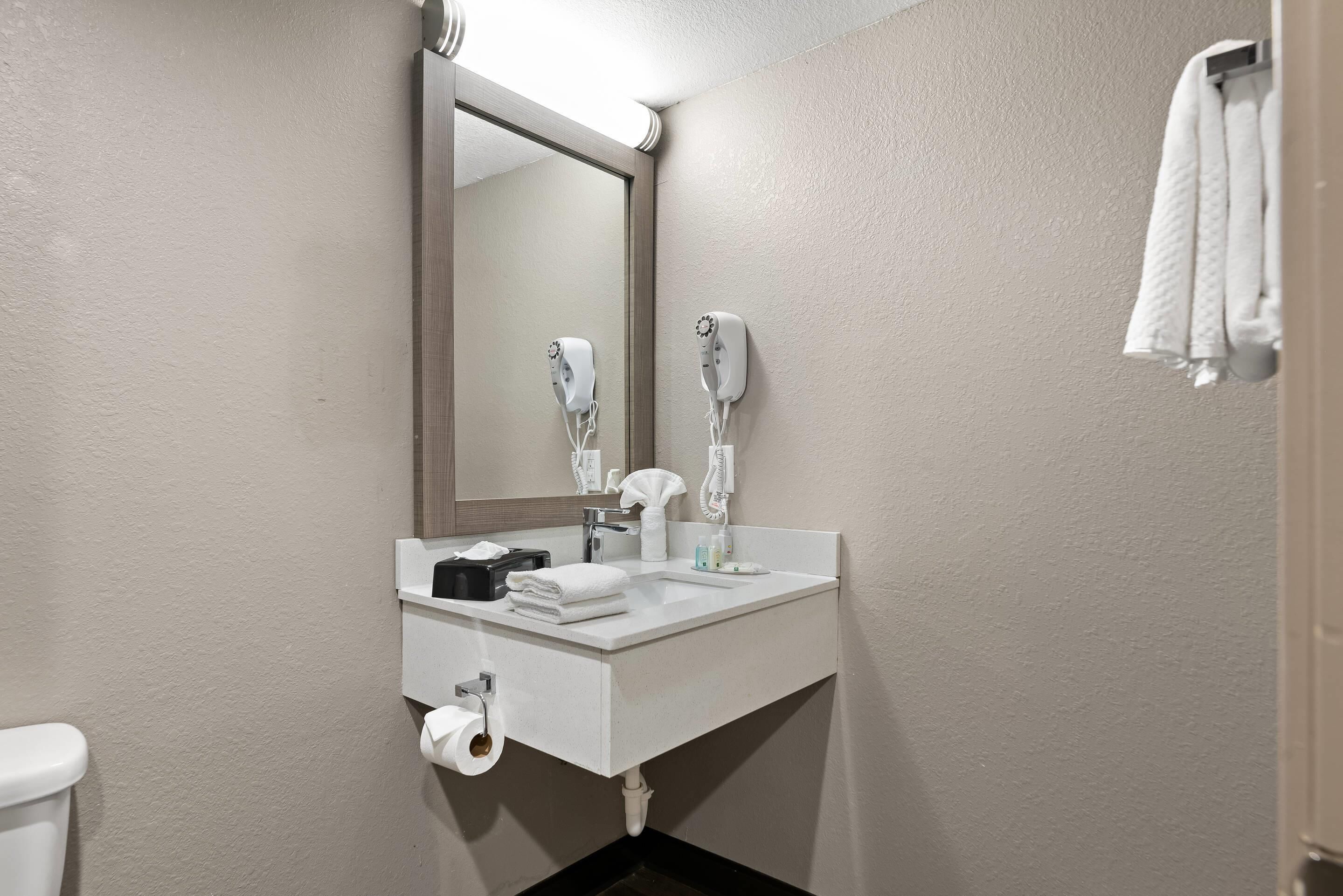 A bathroom with a white sink, two hair dryers, a mirror, a towel rack, and a toilet.