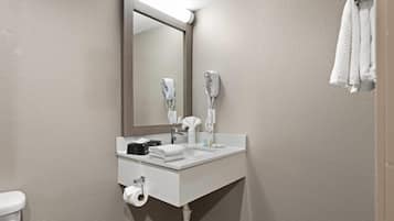 A bathroom with a white sink, two hair dryers, a mirror, a towel rack, and a toilet.