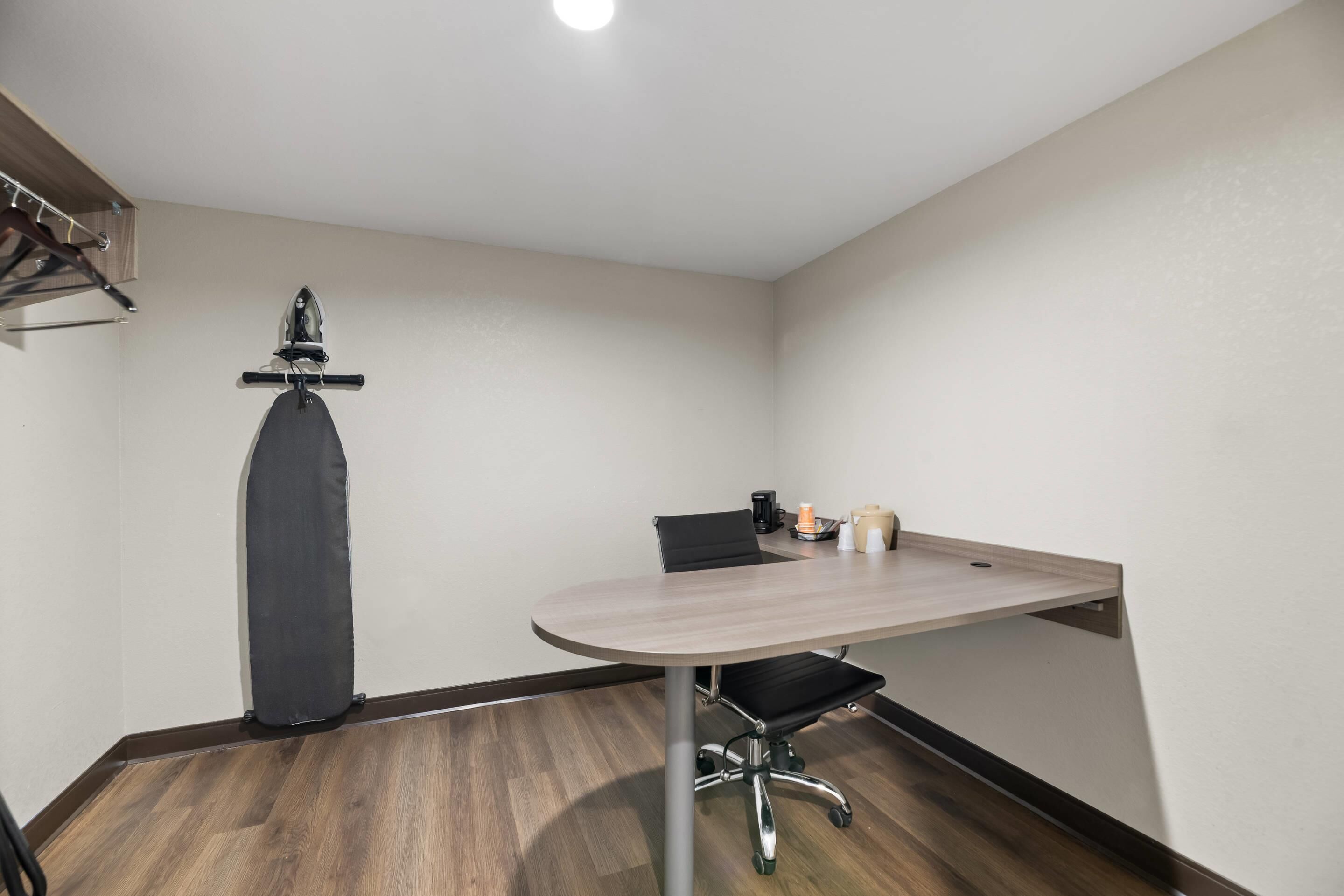 Una sala de conferencias con una mesa redonda, una silla de oficina negra, un plancha vertical y una máquina de café.