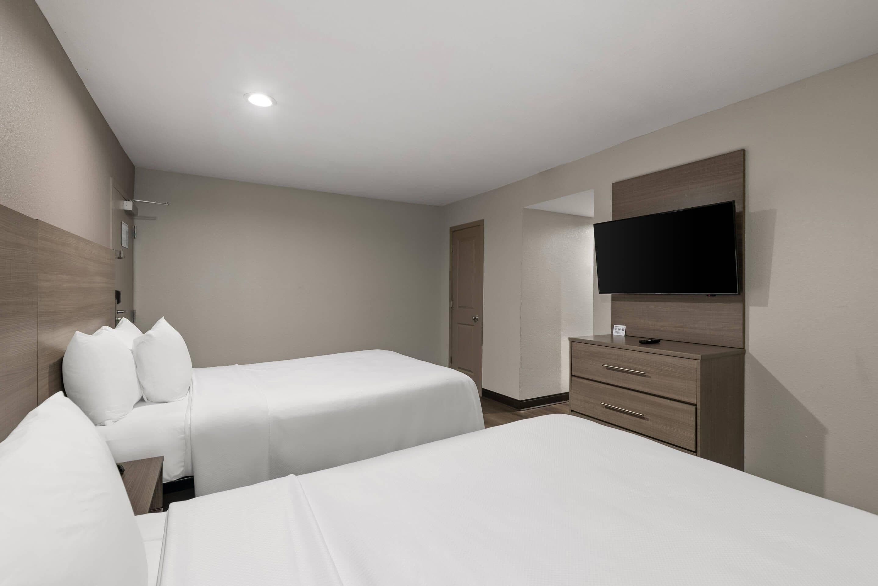 Habitació d'hotel amb dos llits, una televisió, un taulell i una porta.