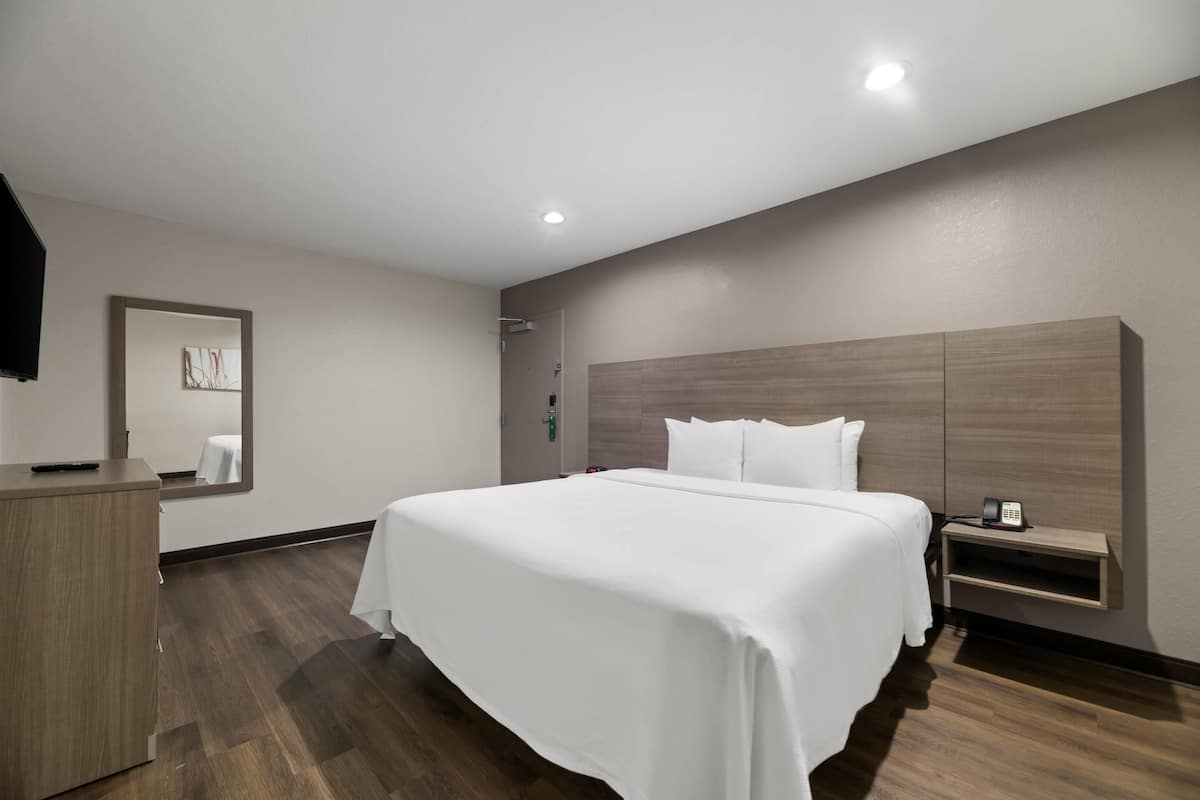 Une chambre d’hôtel avec un grand lit, une table de chevet en bois, un miroir et une tête de lit en bois.