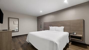 A hotel room with a large bed, a wooden nightstand, a mirror, and a wooden headboard.