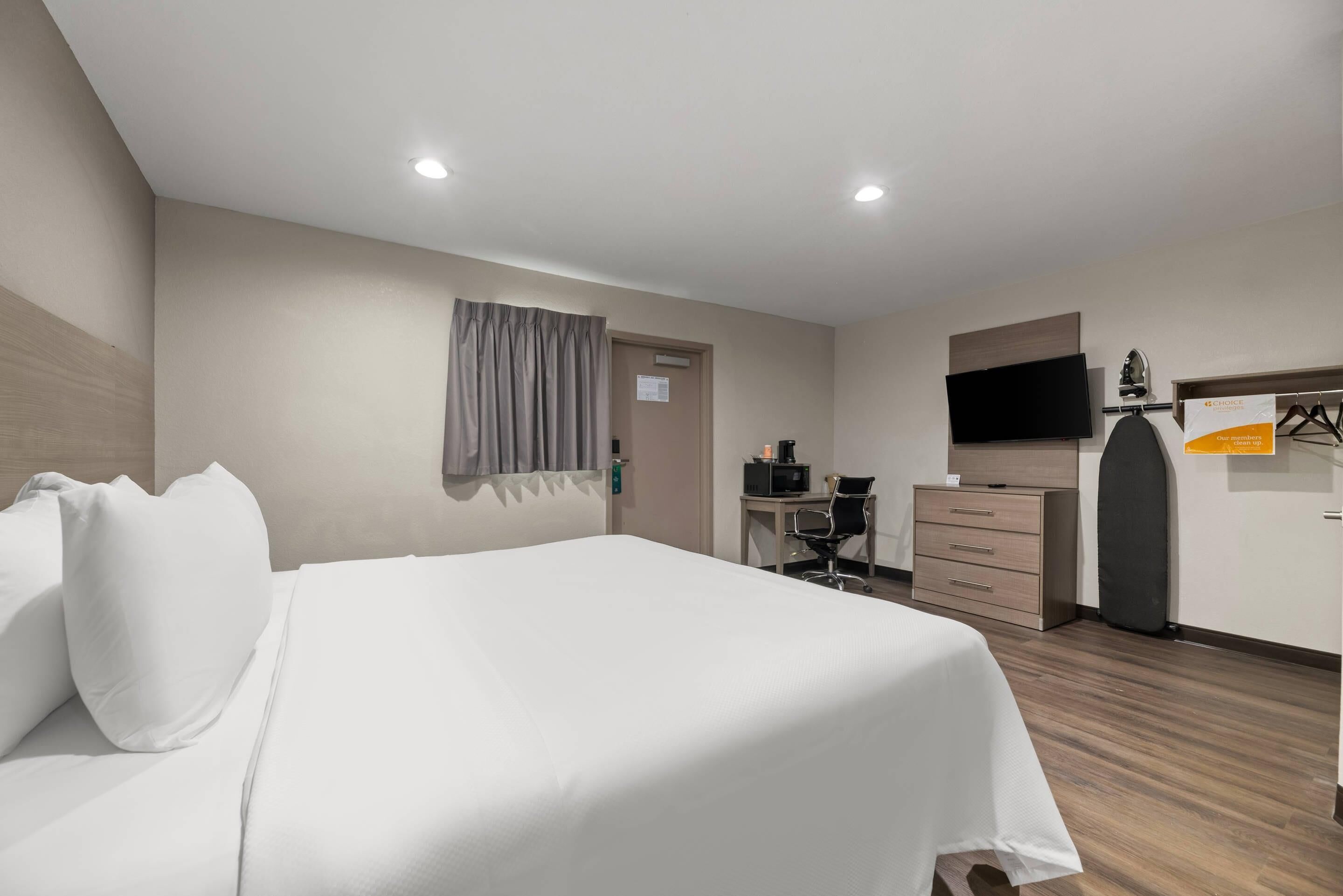Une chambre d’hôtel comprenant un lit, un bureau, une chaise, une télévision et une armoire.