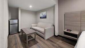 A compact living space with a sofa, a small table, a built-in TV shelf, and a refrigerator. - Quality Suites Wildwood - The Villages (Wildwood)