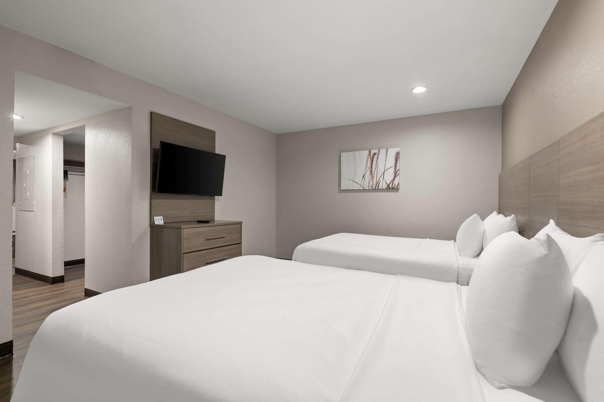 A hotel room with two beds, a TV mounted on the wall, a wooden cabinet, and a painting on the wall.