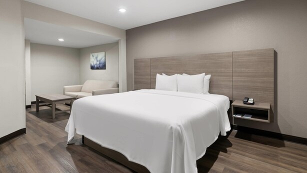 A hotel room with a large bed, a sofa, a small table, a nightstand with a phone, and a painting on the wall. - Quality Suites Wildwood - The Villages (Wildwood)