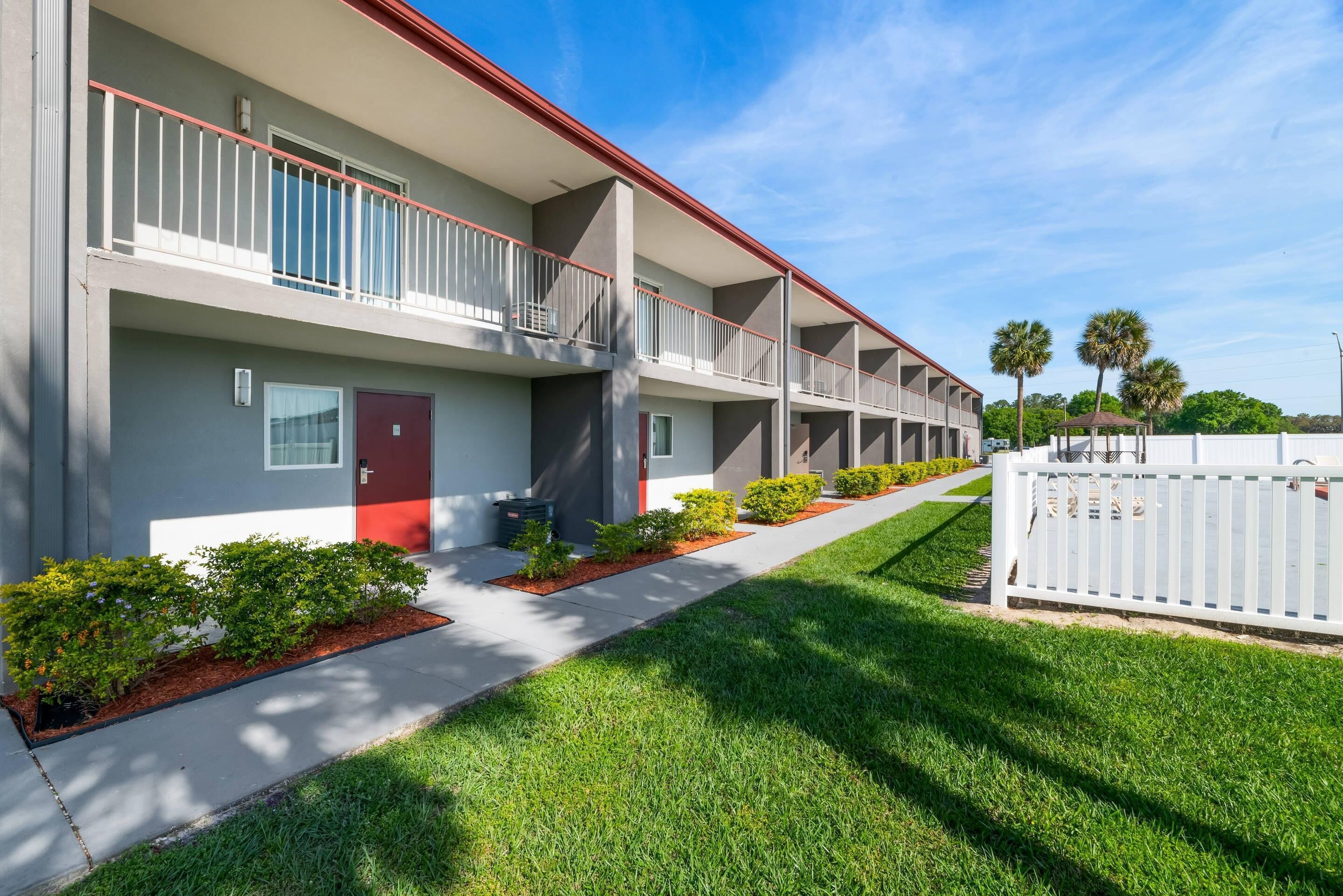 A multi-story hotel with balconies, a red door, and a well-maintained lawn.