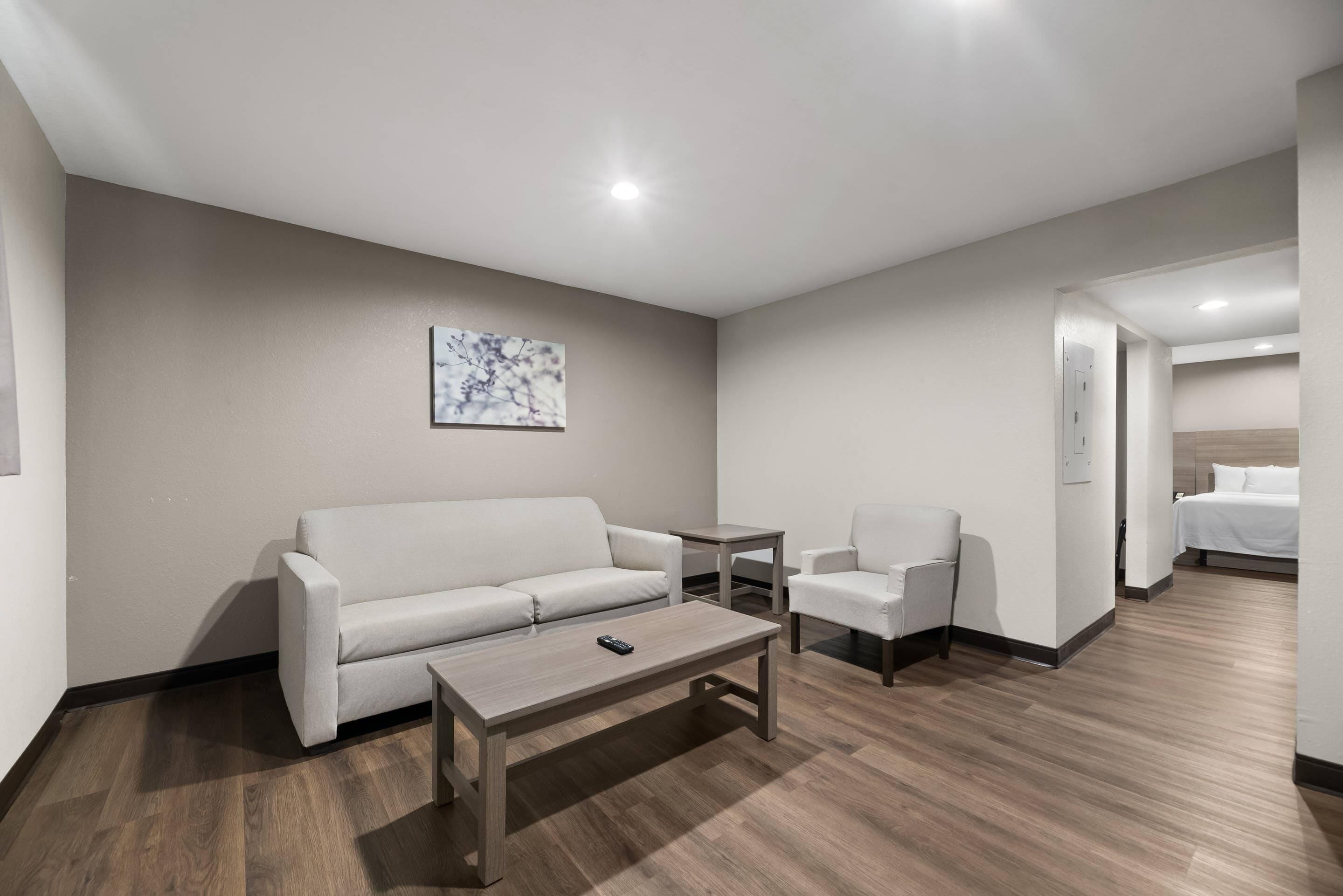 A modern hotel room with a white sofa, a small table, a chair, and a bed.