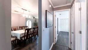 Un pasillo que conduce a un comedor con una mesa y sillas, un cuadro en la pared y una puerta al final.