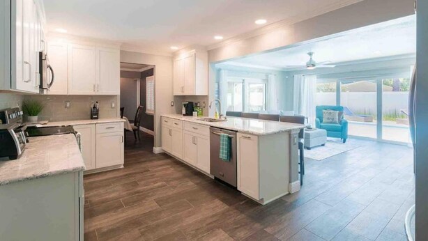 Una cocina moderna con armarios blancos, una isla central y un comedor con una silla azul.