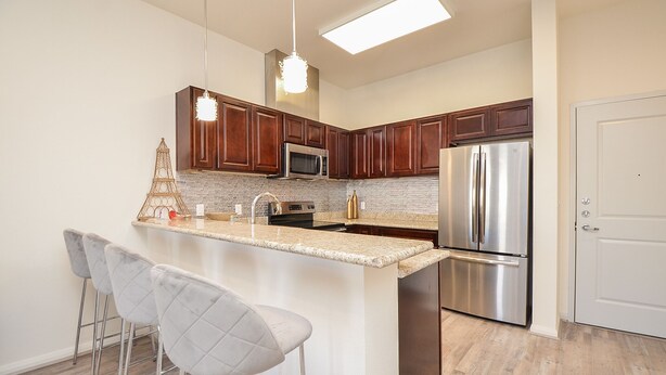 A modern kitchen with a central island, stainless steel appliances, and a bar area with stools. - 1D | Gated Complex | Daily Needs in Walking Distance  (Katy)