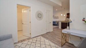 A modern living room with a white sofa, a desk with a lamp, and a decorative mirror on the wall. - 1D | Gated Complex | Daily Needs in Walking Distance  (Katy)