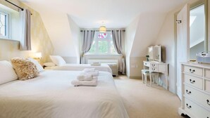 Une chambre avec deux lits, une commode, une coiffeuse et une fenêtre avec des rideaux.