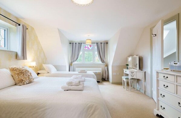 A bedroom with two beds, a dresser, a vanity, and a window with curtains.