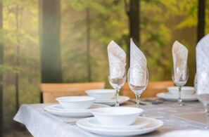 Una mesa dispuesta con platos blancos, cuencos y cristalería transparente, sobre un fondo natural desenfocado.