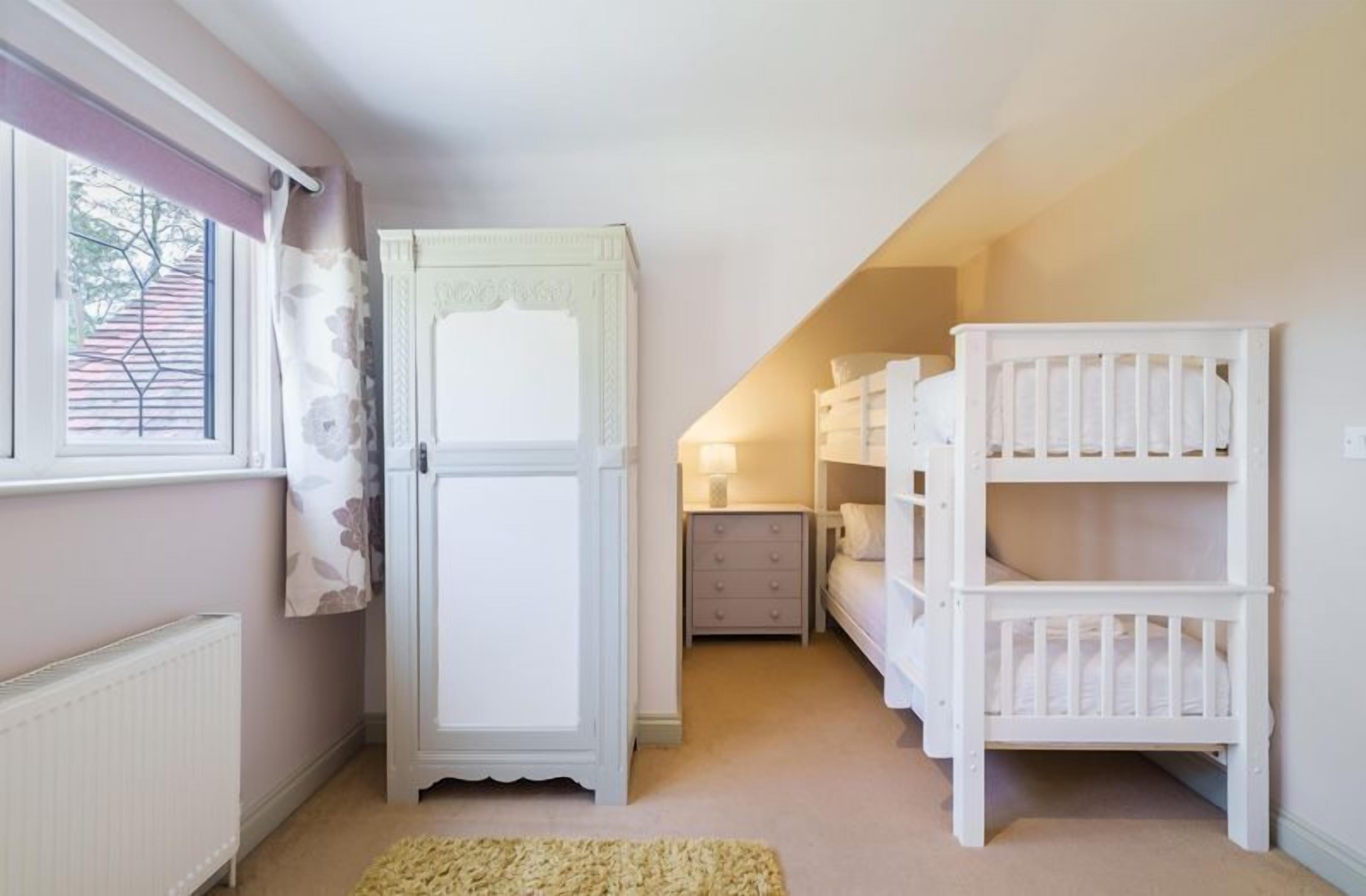A child's room with bunk beds, a wardrobe, a radiator, and a window with curtains.