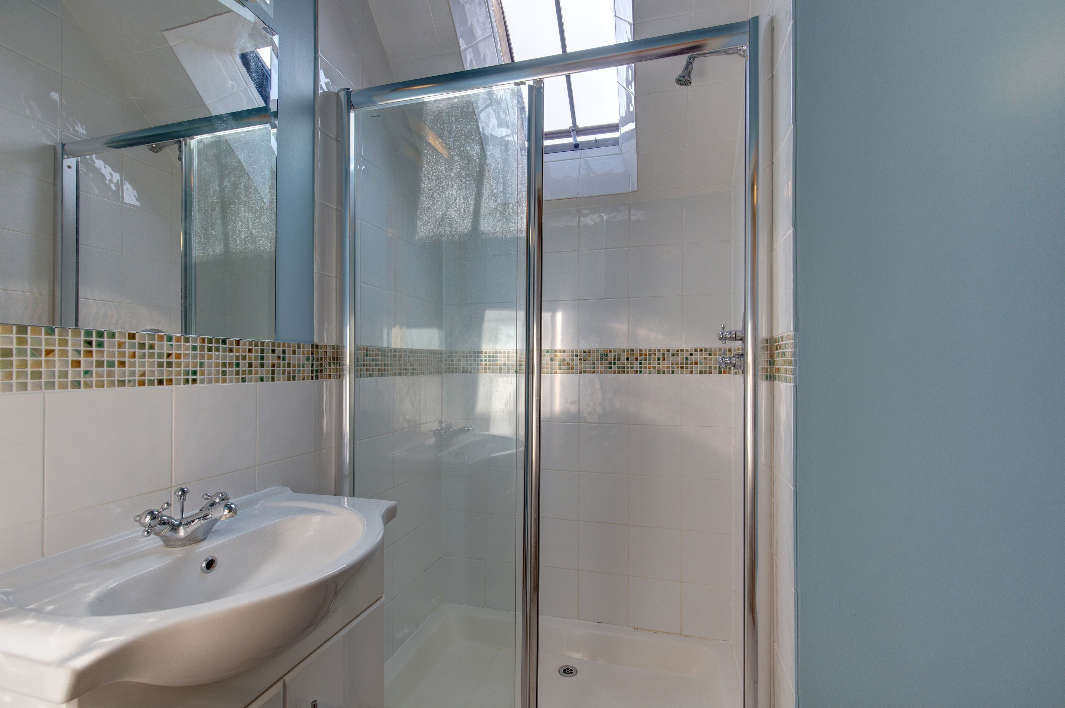 Une salle de bain avec une douche à parois de verre, un lavabo blanc et un mur recouvert de carreaux.