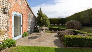 A patio with a table and chairs, a stone wall, and a well-maintained hedge.