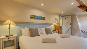 A neatly made bed with pillows and a rolled towel, a bedside table with a lamp, and a painting on the wall.