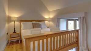 Un dormitorio con una cama de madera, dos lámparas de noche, un ventanal con cortinas y una barandilla de madera.