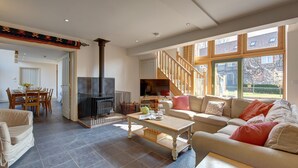 Amplia sala de estar con chimenea, un juego de sofás, una mesa de comedor y una escalera que conduce a un nivel superior.