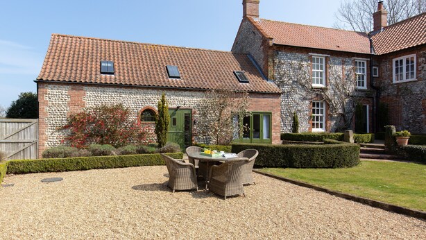 A stone building with a tiled roof, a gravel patio, and wicker furniture. - Riding Stable - sleeps 6 guests  in 3 bedrooms (Holt)