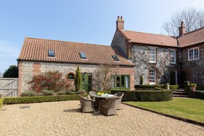 A stone building with a tiled roof, a gravel patio, and wicker furniture. - Riding Stable - sleeps 6 guests in 3 bedrooms (Holt)